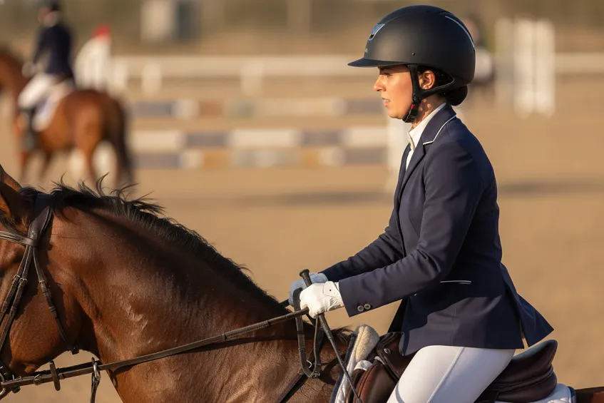 Casque équitation : un cavalier à cheval portant un casque moderne correctement ajusté, la jugulaire attachée et visible, vu de côté.