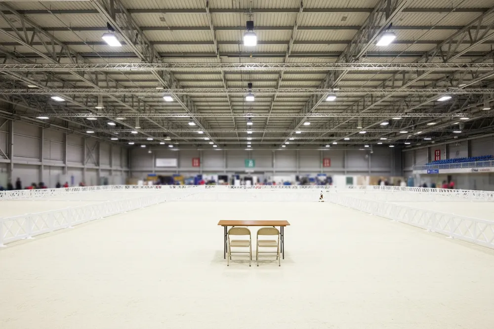 Hall d'exposition canine couvert, rings délimités par des barrières basses sur un sol clair.