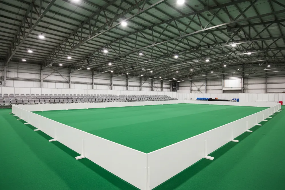 Un ring d'exposition canine installé dans un hall couvert, tapis vert et barrières basses